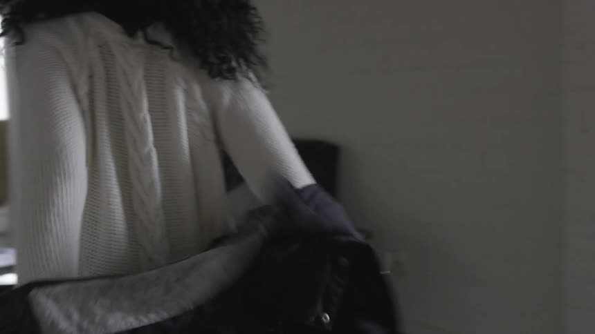 A woman walks into her home and removes her coat