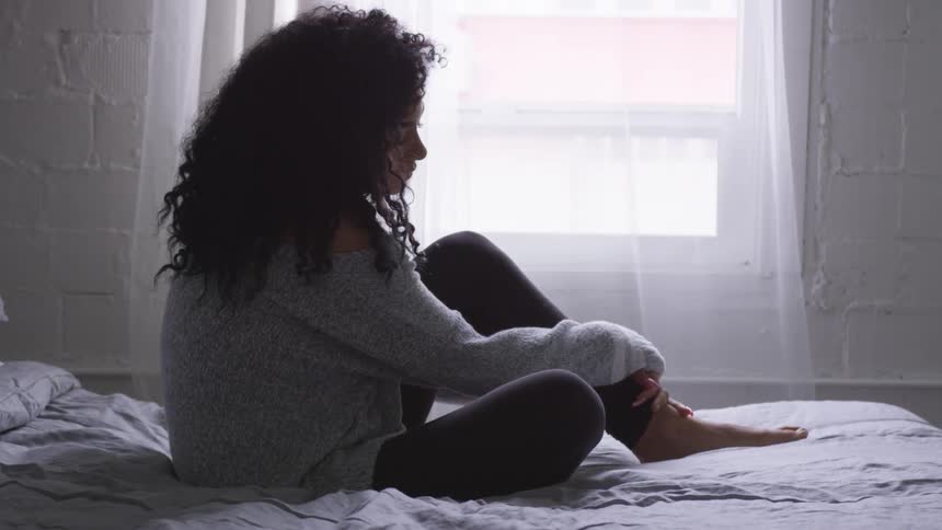 A woman sitting on the bed looking out the window