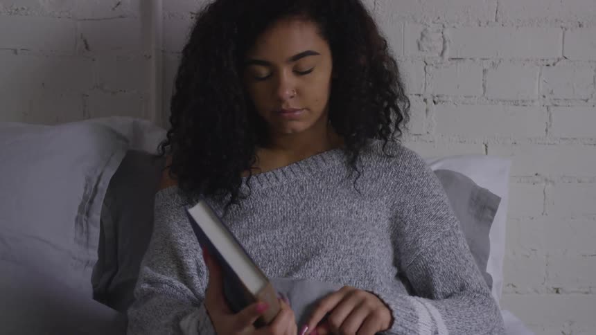 A woman sitting up reading in bed closes her book and sighs