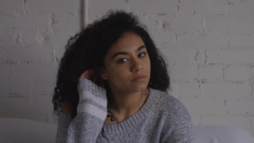 A woman stares into the camera as she moves her hair behind her ear