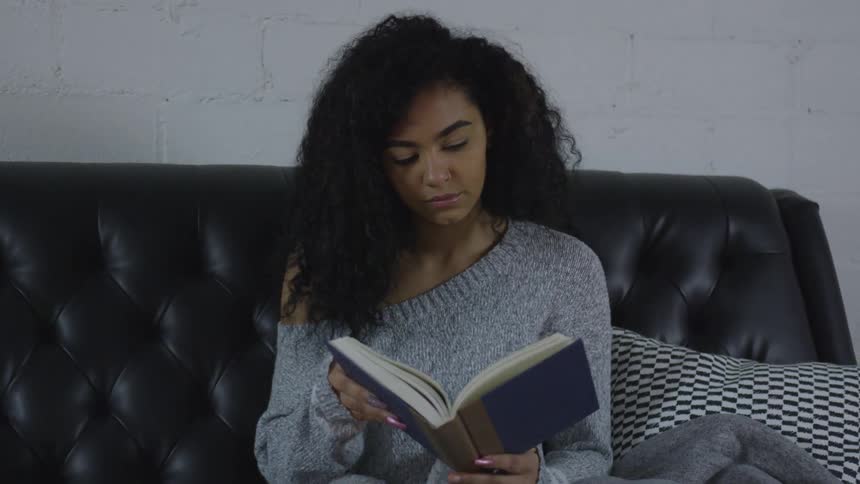Woman looks at a book as she sits on a leather sofa