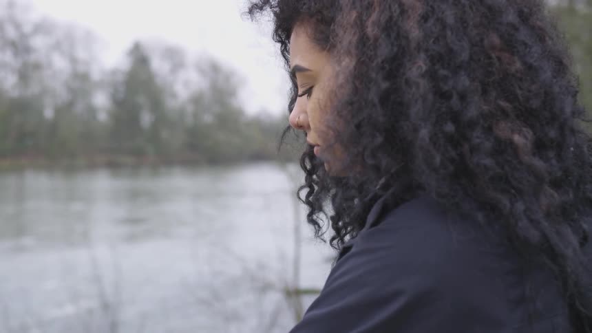 A woman sitting in front of a pond thinking