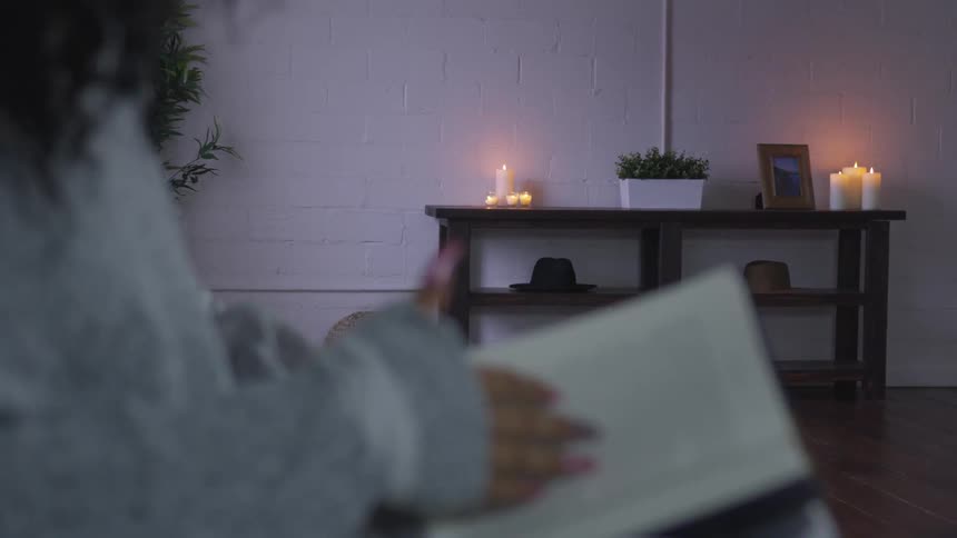 Black woman sits down and turns over page indoors at dusk