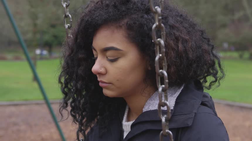 Curly hair brunette girl sits on the swing on the playground during daylight