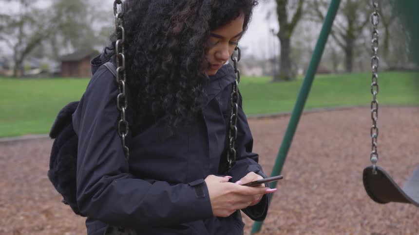 A woman sits on a swing and texts on a mobile phone
