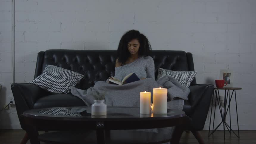 Woman sits on the black sofa and reads book at home