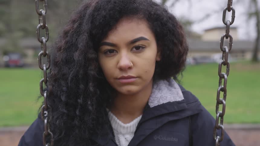 Curly hair brunette girl wearing nose ring sits on the swing on a cloudy day