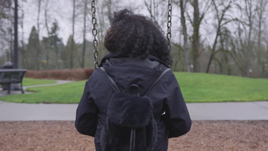 A black woman sits on a swing in a park