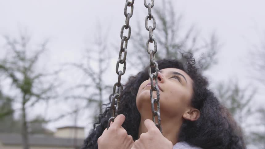 A woman with curly hair looks up at the sky while spinning in a swing