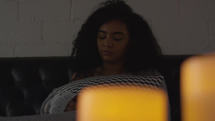 A young woman preens and hugs a cushion while sitting on a sofa