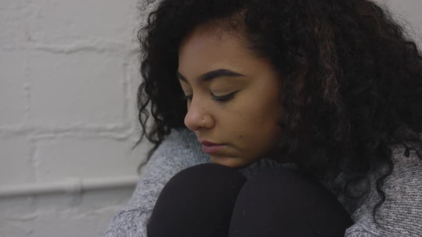 A black woman kneels against a wall