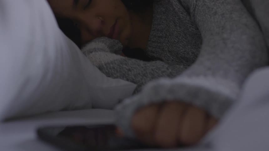 A woman in bed reaches for her phone