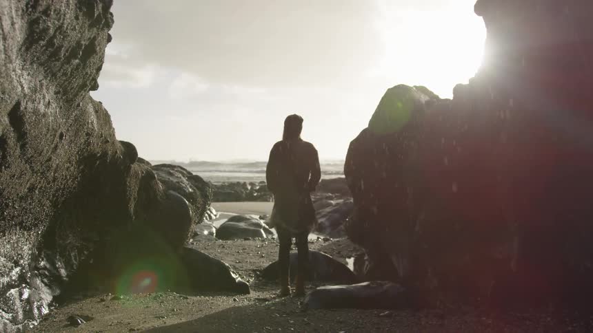 A person stands on a rocky beach in the rain