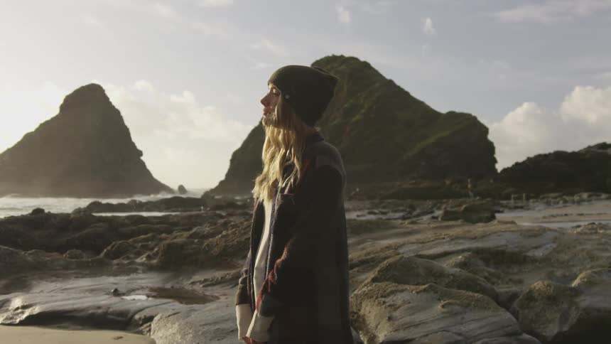 A woman stands on a rocks coast line