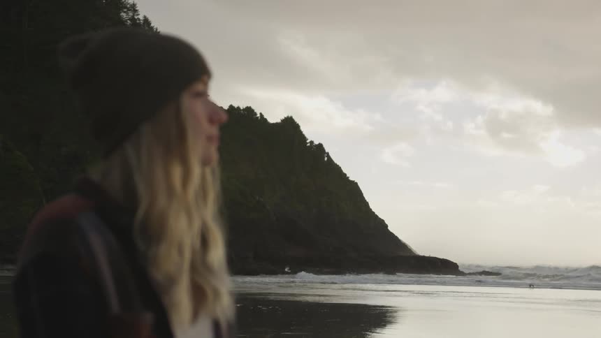 A woman stares into a rough ocean surrounded by hills and rocks