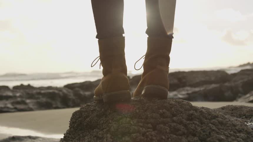 Woman wearing boots stand on rock while the sun goes down