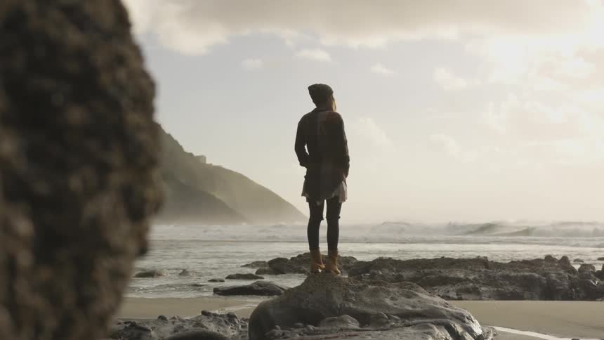 A woman standing on top of a rock at a beach