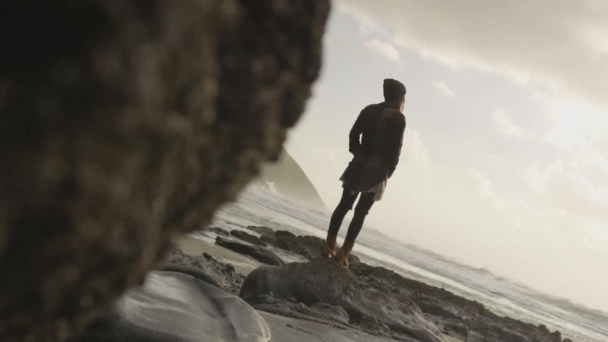 A woman standing on rocks next to the ocean