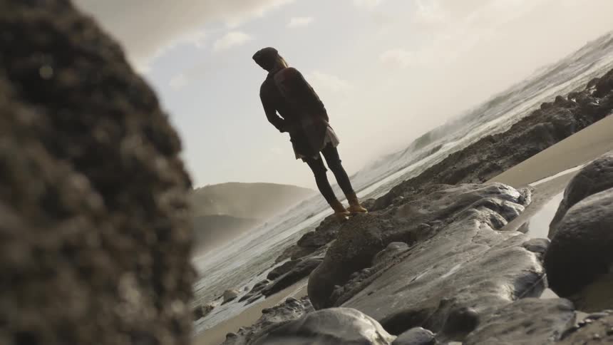 Woman stands on a rock as she looks out at the ocean
