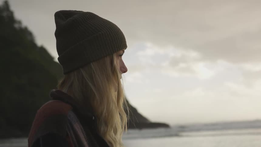 A woman stands next to the ocean and looks over the water