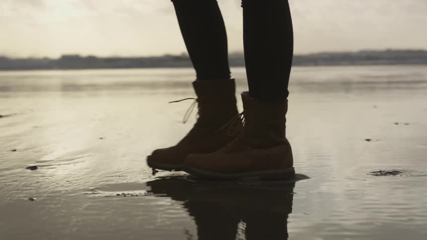 A woman wearing hiking boots walking through wet sand