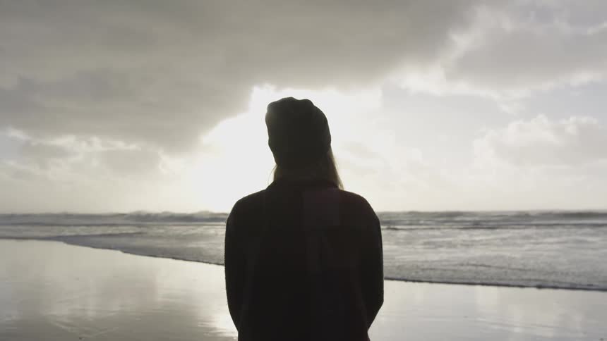 Woman stands on the beach looking out at the water