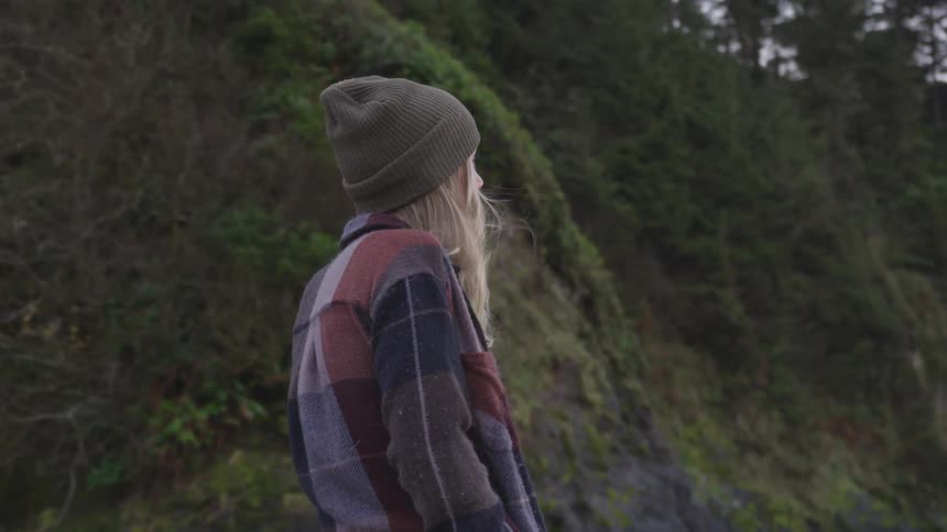 A woman is walking next to the bottom of a grassy cliff