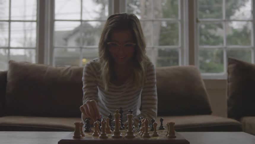 Young woman in glasses plays chess on a couch