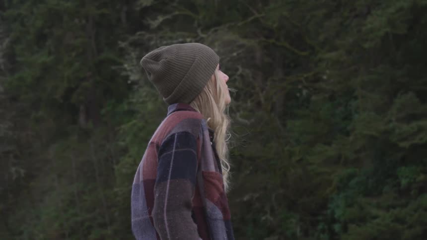 Blonde woman wearing wooly hat looks around in the forest by day