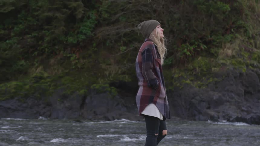 A woman walks along the river and looks up toward the sky