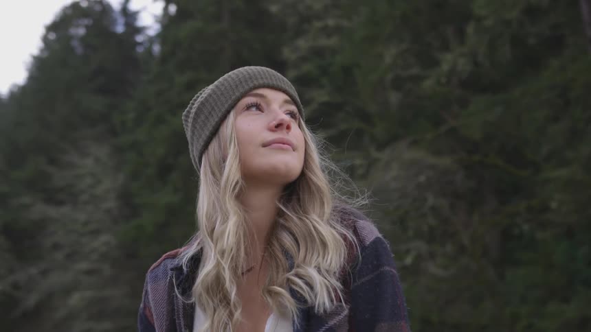 A young blonde woman turns around to face a forest in daylight