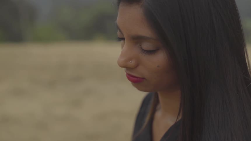A young woman sits in a field with her eyes closed
