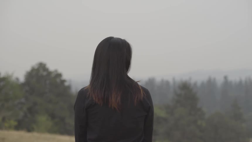 A woman stands on a slope and looks at the trees and sky