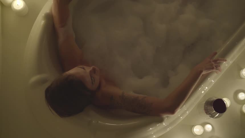 A woman lays in a bubble bath surrounded by candles