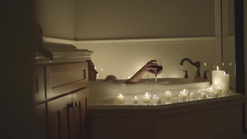 A lady has a bath with candles and wine