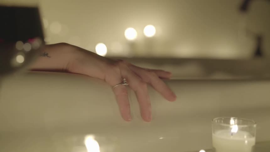 A woman's hand on the rim of a bathtub with candles and a glass of wine