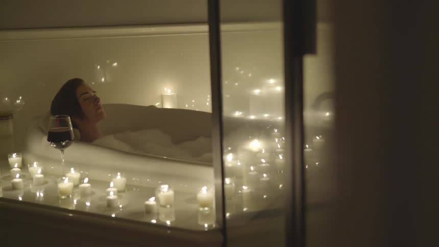 Woman soaks bubble bath surrounded by candles