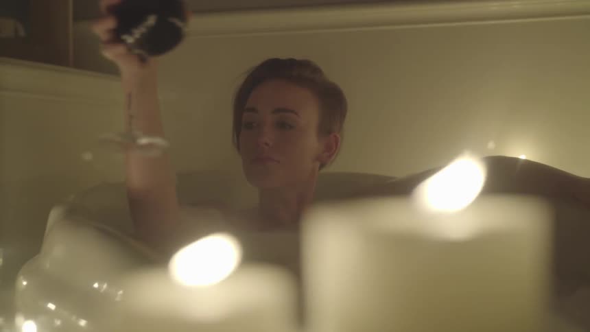 Woman sips the wine from a glass while taking a bath