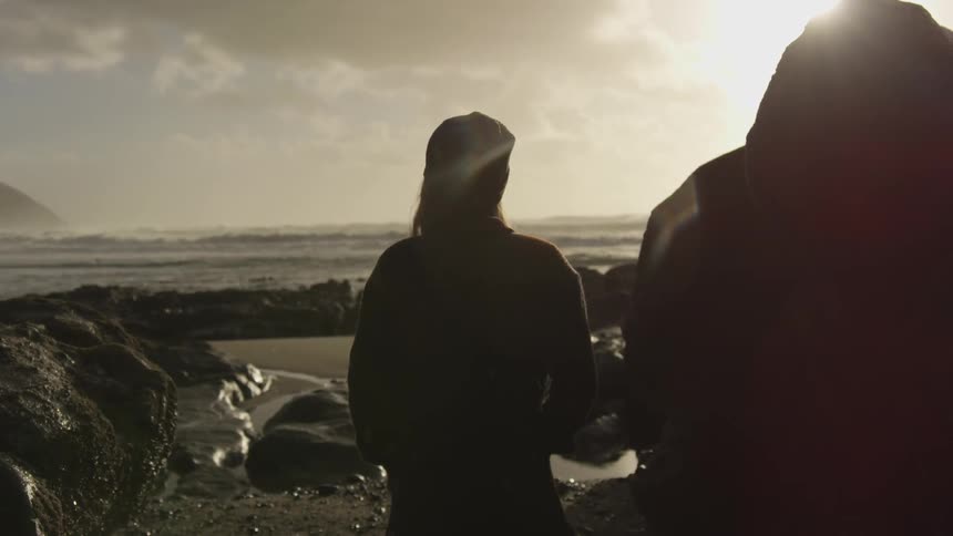 Silhouette of a woman standing on a rocky beach in light rain