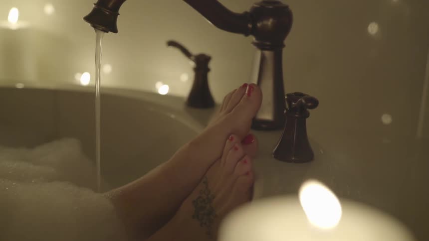 A woman in a candle lit bathtub full of bubbles