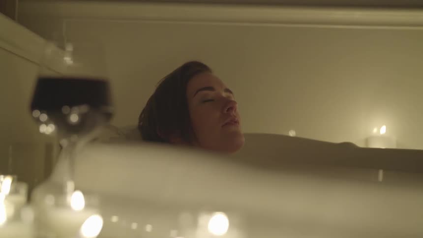 A woman relaxes in a bath with small candles and a glass of wine
