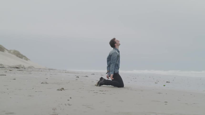 A man falls to his knees on the beach
