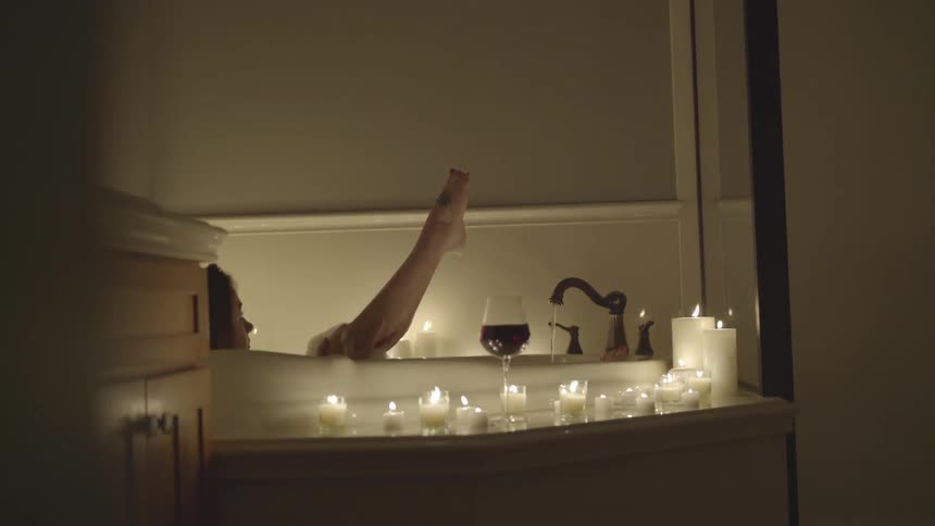 A woman takes a bubble bath with a glass of wine