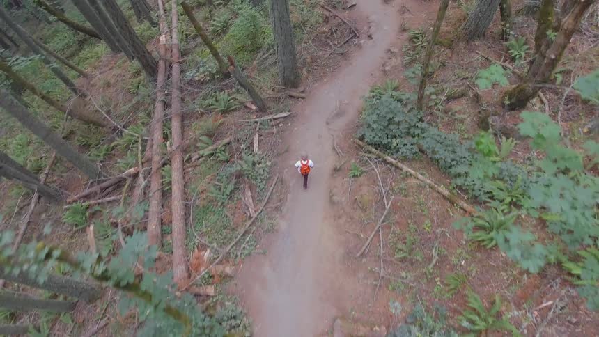 A person wearing a backpack walking down a paved path in the woods