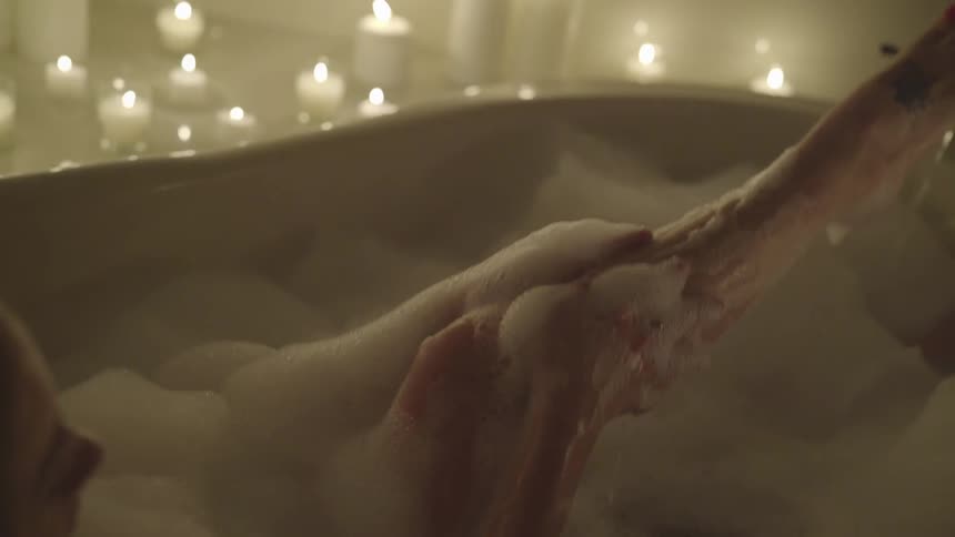 A white woman in a bathtub soaps up her leg