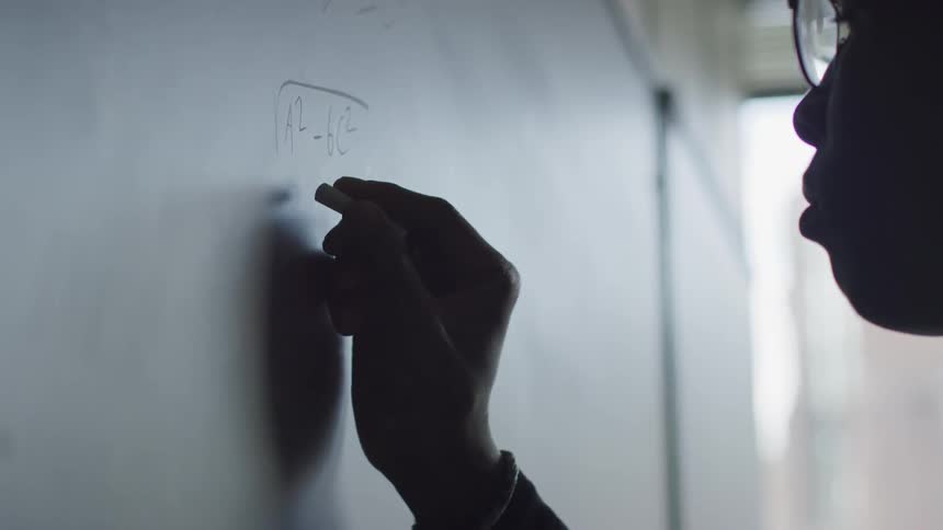 A black man draws a math equation on a chalkboard