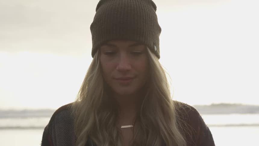 A woman in a winter cap stands outside in the rain at sunset