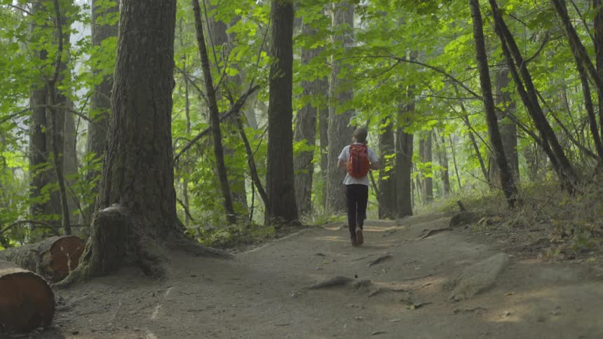 A teenage boy wearing a backpack walks on a path through a forest