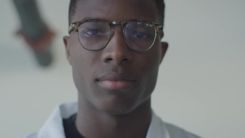 A young black man in glasses looks forward with a peaceful and intelligent gaze