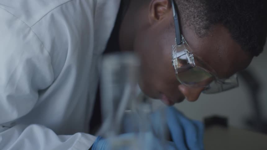 A male scientist takes notes in a lab while wearing safety glasses